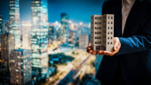 Una mujer de negocios presenta una maqueta detallada de un edificio con el animado perfil urbano de fondo; promoción inmobiliaria, estabilidad de la inversión, potencial de ingresos por alquiler y revalorización de los inmuebles.